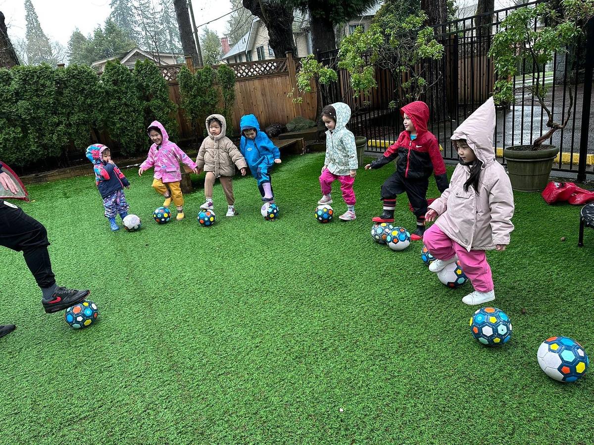 Children in rain jackets playing with soccer balls in the school’s outdoor play area